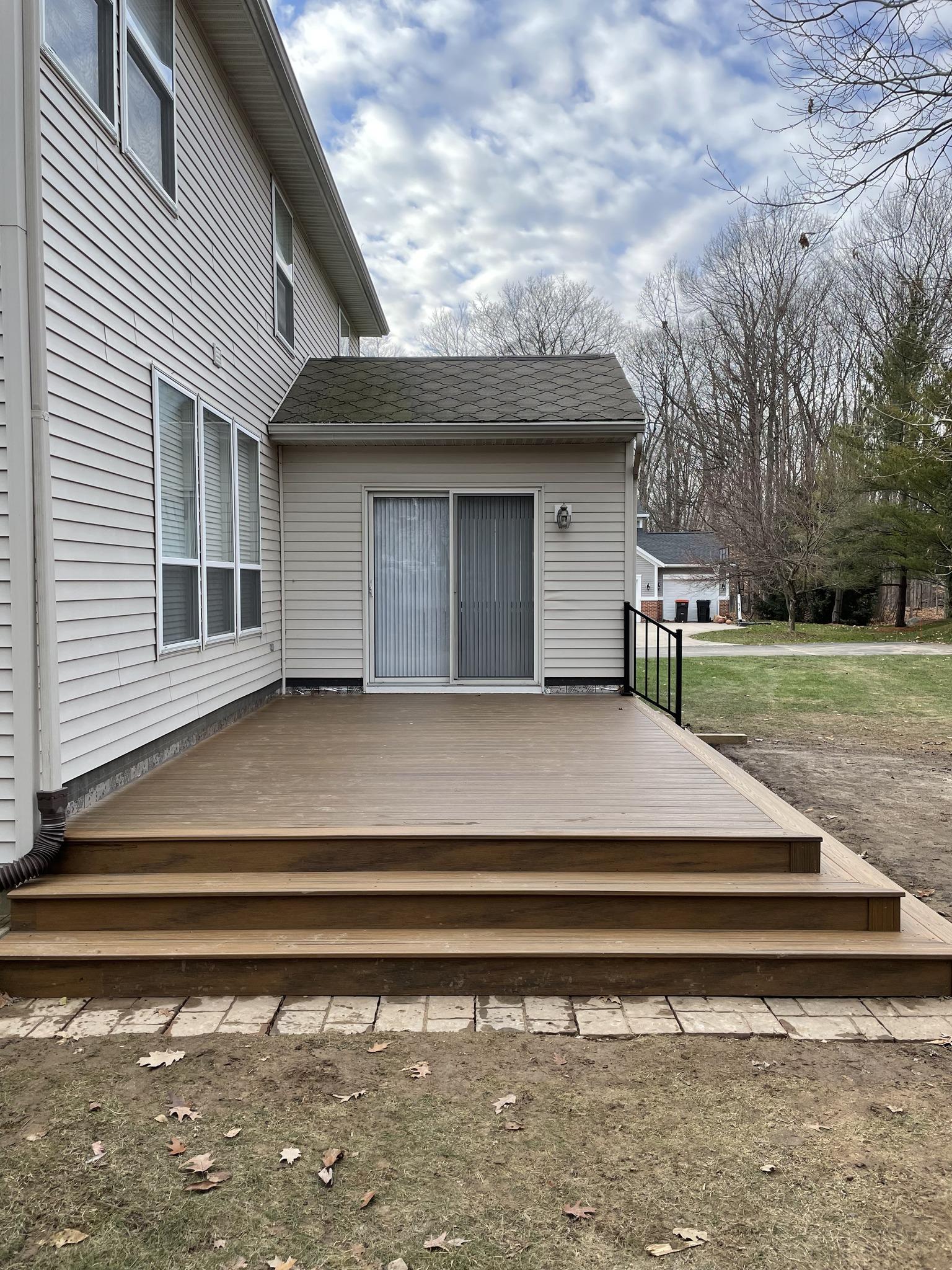 Ground-level composite deck with wide steps and paver border at rear of home