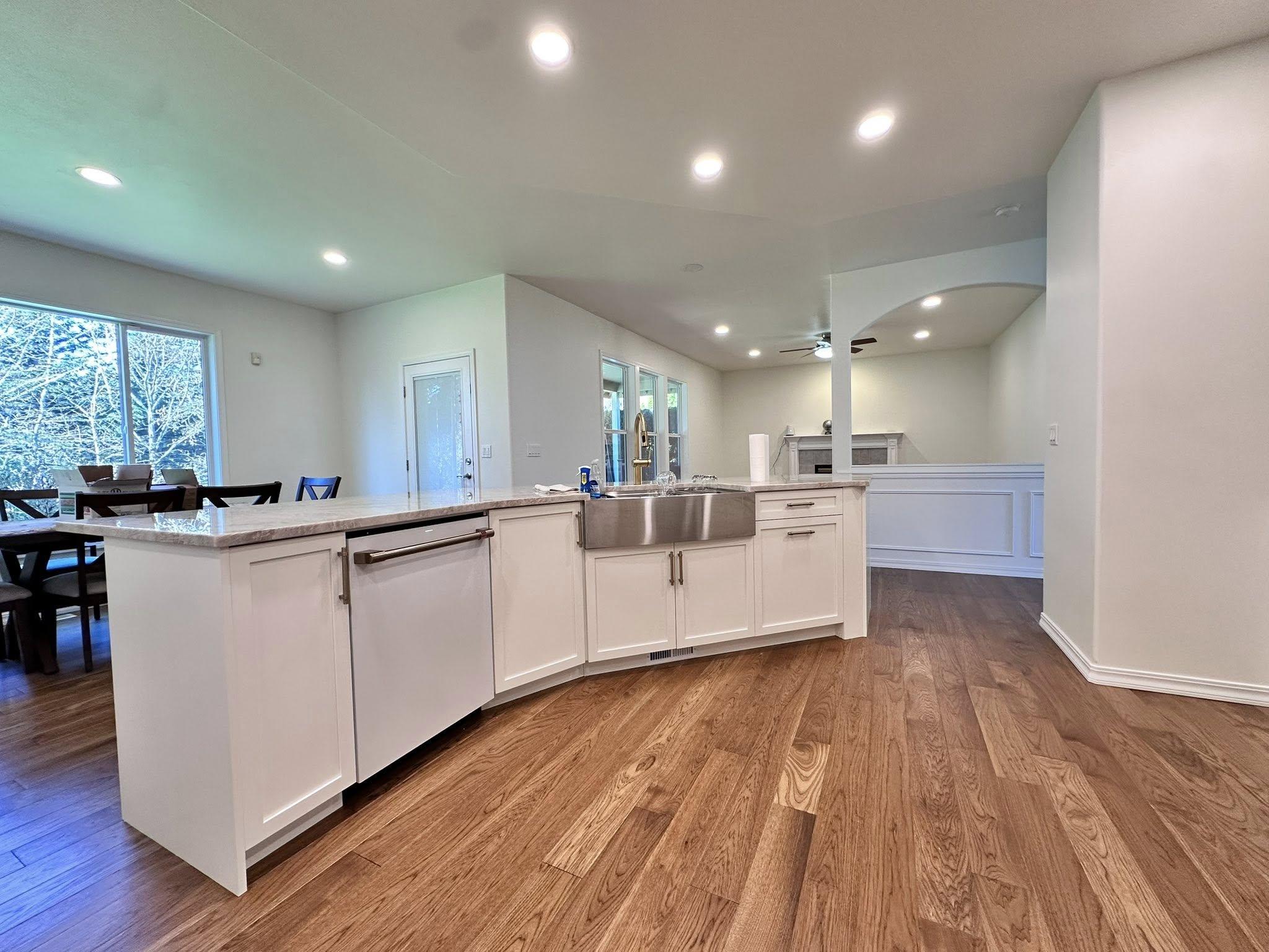 Spacious kitchen renovation with white cabinetry, farmhouse sink, open floor plan to dining area, and hardwood floors