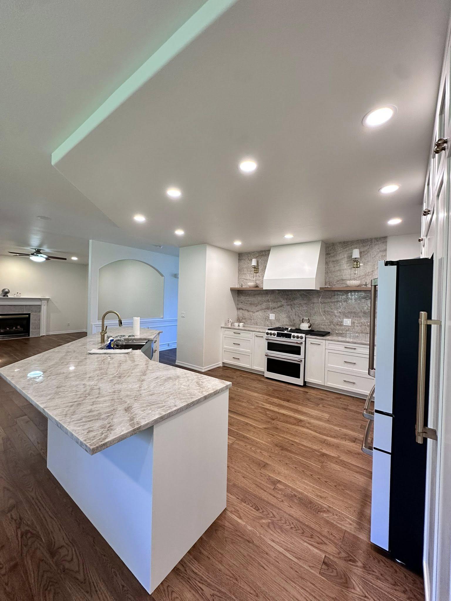 Kitchen remodel featuring marble island countertop, professional range with ventilation hood, and open layout to living area